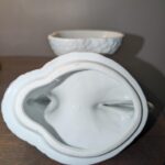 Underside view of vintage white porcelain rooster covered candy dish lid showing clean glaze and rim detail, with base bowl visible in background